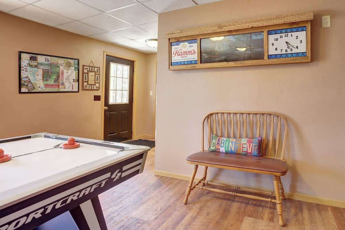 Une pièce comprenant une table de billard, une chaise en bois avec un coussin, une horloge encadrée et un tableau d’affichage où divers objets sont accrochés.
