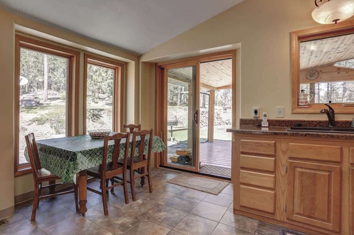 A dining area with a table and chairs, a kitchen with wooden cabinets and a countertop, and large windows offering a view of the outdoors.