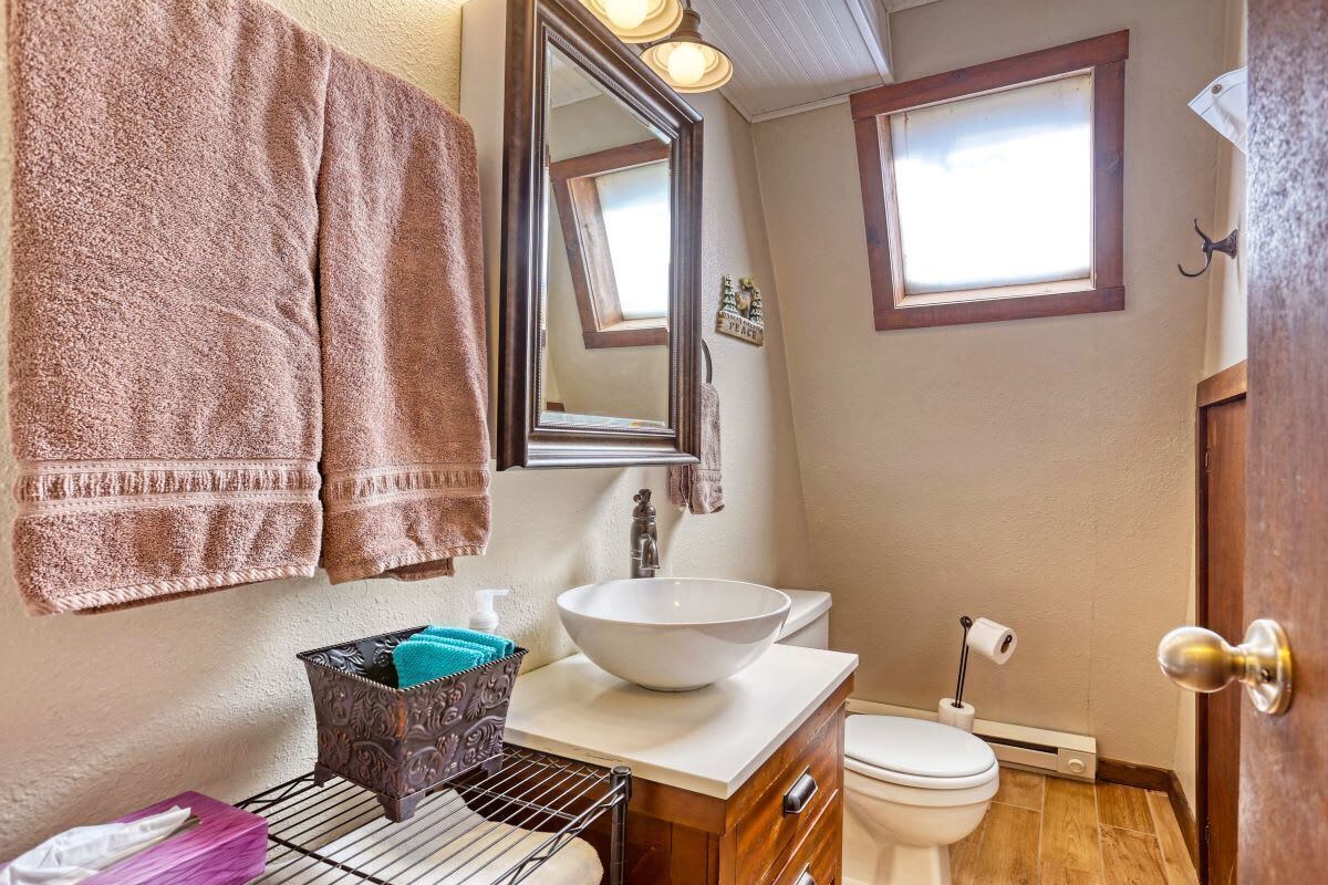 A bathroom with a white sink, a toilet, and a mirror. There are towels hanging on the wall and a small trash bin on the counter.