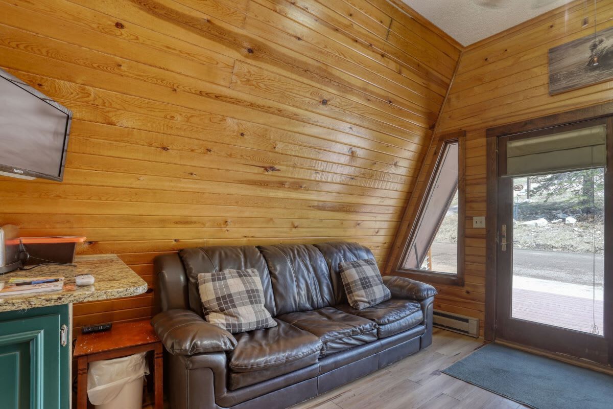 Ein gemütliches Blockhaus-Interieur mit einer Ledersofa, Holzwänden, einem Fernseher und einem Fenster mit Blick auf eine felsige Landschaft.