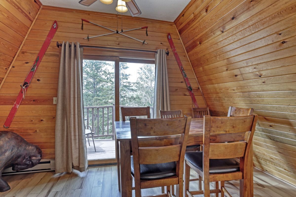 A wooden cabin with a dining area, a large window, and a ski rack.