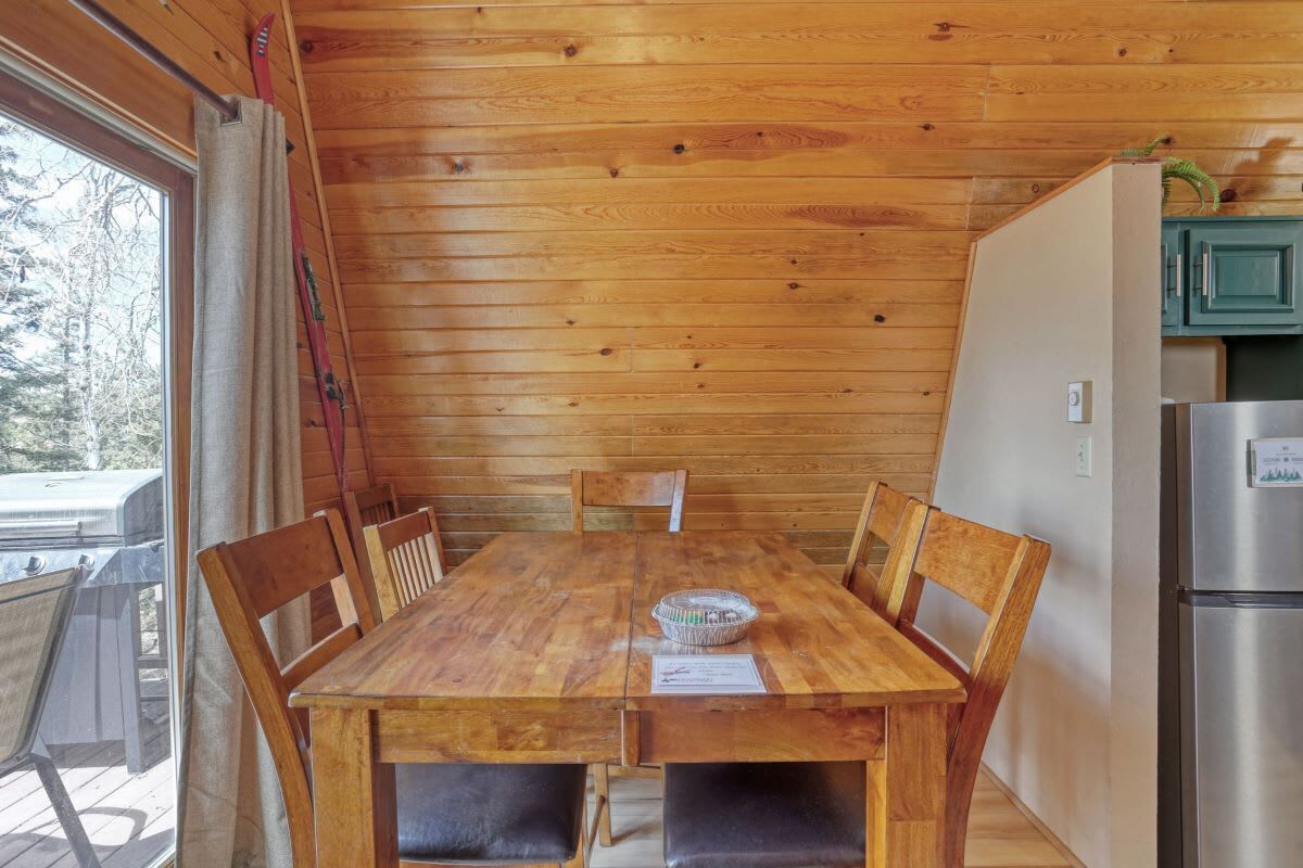 Een houten eettafel met stoelen, een mand en een koelkast in een kamer in chaletstijl, met houten wanden en plafond.