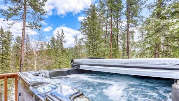 Een hottub in een bebost gebied met een houten terras en metalen reling.