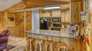 L’intérieur d’une cabane en bois comprend un coin cuisine équipé de meubles de rangement en bois, d’un réfrigérateur, d’un four à micro-ondes et d’un comptoir-bar avec des tabourets.