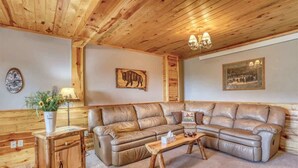 Un salon chaleureux avec un grand canapé en cuir en forme de L, des tables d’appoint en bois et un lustre.
