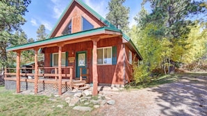 A wooden cabin with a porch and a covered deck, surrounded by trees and a gravel path. - Cozy Black Hills Retreat – Loft, deck, pet-friendly & peaceful mountain views! (Lead)