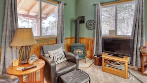 A cozy living room with a leather chair, a TV on a wooden stand, a fireplace, and a lamp on a side table. - Cozy Black Hills Retreat – Loft, deck, pet-friendly & peaceful mountain views! (Lead)
