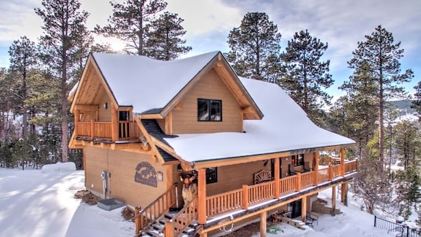 A wooden cabin with a balcony, a staircase, and a snow-covered roof, surrounded by trees. - Wannabee Moose Lodge (Sturgis)