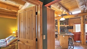 A cozy cabin interior with a wooden door, a kitchen area with a stone wall, and a bar stool. - Wannabee Moose Lodge (Sturgis)