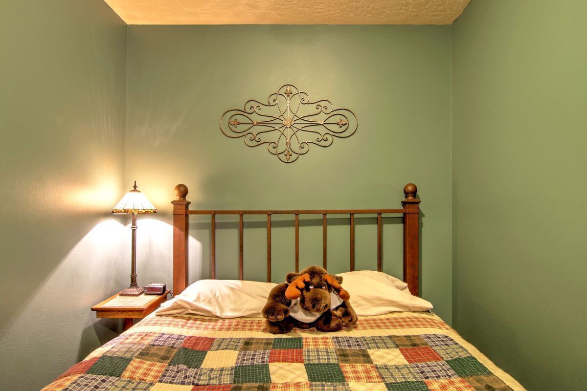 Ein Schlafzimmer mit einem Bett, einer Wanddekoration, einem Nachttisch mit Lampe und einem Stofftier.