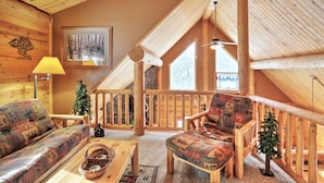 A cozy log cabin interior with a wooden ceiling, a fireplace, a sofa, a chair, and a small Christmas tree. - Wannabee Moose Lodge (Sturgis)