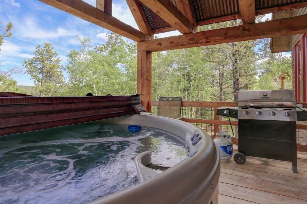 A hot tub on a wooden deck with a grill and propane tank nearby.