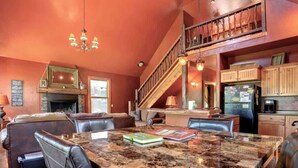 A spacious living area with a large marble table, leather seating, a fireplace, and a kitchen with wooden cabinets and a staircase. - Mercantile Cabin (Lead)