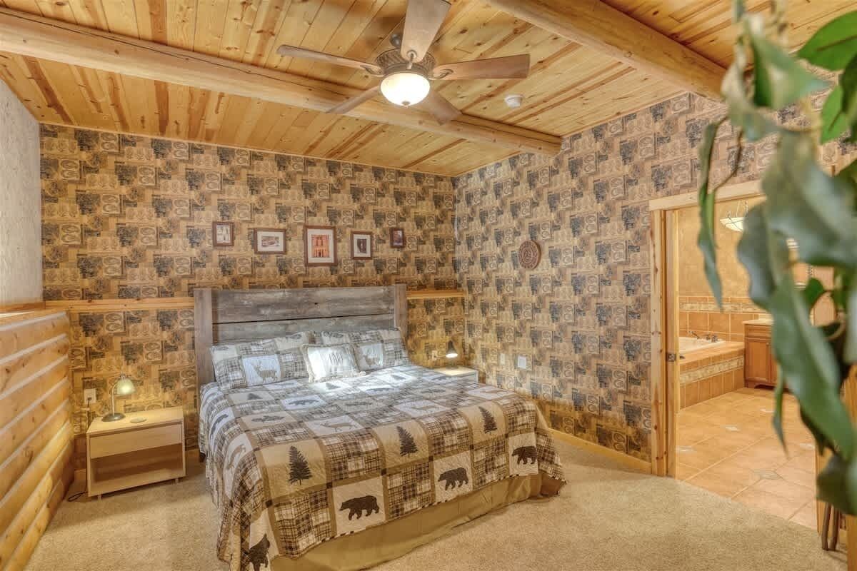 Une chambre avec un plafond en bois, un lit recouvert d’une couvre-lit à motifs et un ventilateur de plafond.