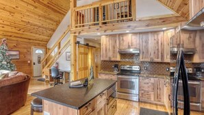 A spacious kitchen with wooden cabinets, a central island, and a staircase leading to an upper level. - Great Pine Lodge (Lead)