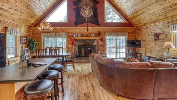 A log cabin interior with a dining area, fireplace, and a large leather couch. - Great Pine Lodge (Lead)