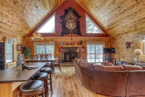 A log cabin interior with a dining area, fireplace, and a large leather couch. - Great Pine Lodge (Lead)