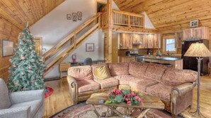 A cozy cabin interior with a wooden staircase, a living room with a sofa and a coffee table, and a kitchen area. - Great Pine Lodge (Lead)