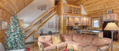 Ein gemütliches Blockhaus-Interieur mit einer Holztreppe, einem Wohnzimmer mit Sofa und Couchtisch sowie einer Küchenzeile.