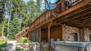 A log cabin with a stone exterior, a wooden deck, and a hot tub. - Great Pine Lodge (Lead)