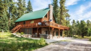 A log cabin with a green roof, a stone chimney, and a porch with a railing. - Great Pine Lodge (Lead)