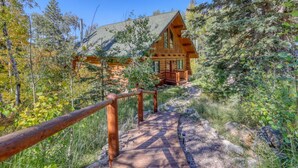 A log cabin with a wooden deck leading to the entrance, surrounded by dense forest. - Deer Haven Lodge – Spacious Family Cabin with Hot Tub, Game Room & Scenic Views (Lead)