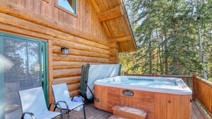 A log cabin with a hot tub on the deck, two chairs, and a covered area. - Deer Haven Lodge – Spacious Family Cabin with Hot Tub, Game Room & Scenic Views (Lead)