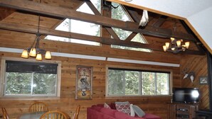 A log cabin interior with a dining area, a red sofa, and a television.