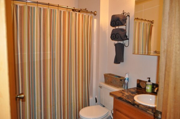 A bathroom with a striped shower curtain, a toilet, a sink with a soap dispenser, and a towel rack.