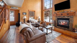 Ein gemütliches Wohnzimmer mit Kamin, Ledersofa und großem Fenster mit Blick auf eine verschneite Landschaft.