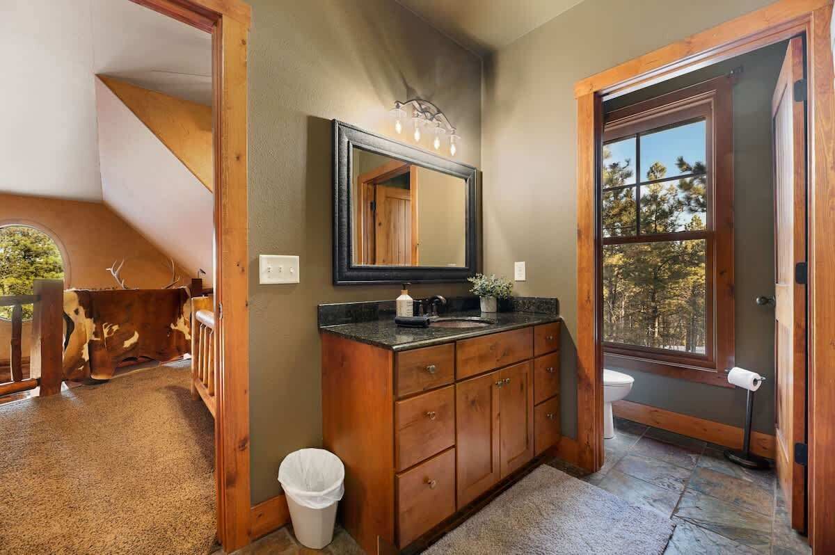 Une salle de bain avec un meuble-lavabo en bois, un grand miroir et une fenêtre donnant sur la forêt.
