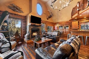 L’intérieur chaleureux d’un chalet avec une cheminée en pierre, des meubles en cuir et une décoration rustique comprenant des bois de cerf et une tête de wapiti.