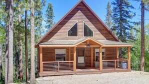A wooden cabin with a triangular roof, large windows, and a porch area. - Lookout View Retreat – Cozy 3-Level Cabin with Hot Tub, Loft & Mountain Views (Lead)