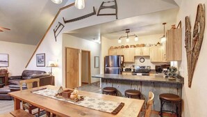 A modern kitchen with wooden cabinets, a stainless steel refrigerator, and a bar area with stools. - Lookout View Retreat – Cozy 3-Level Cabin with Hot Tub, Loft & Mountain Views (Lead)