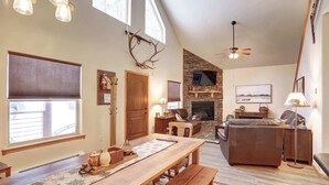 A spacious living room with a fireplace, a dining area with a wooden table, and a large window providing natural light. - Lookout View Retreat – Cozy 3-Level Cabin with Hot Tub, Loft & Mountain Views (Lead)
