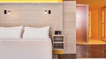 Quarto de hotel moderno com cabeceira de madeira, mesa de cabeceira com rádio e uma cama grande com roupa de cama branca.