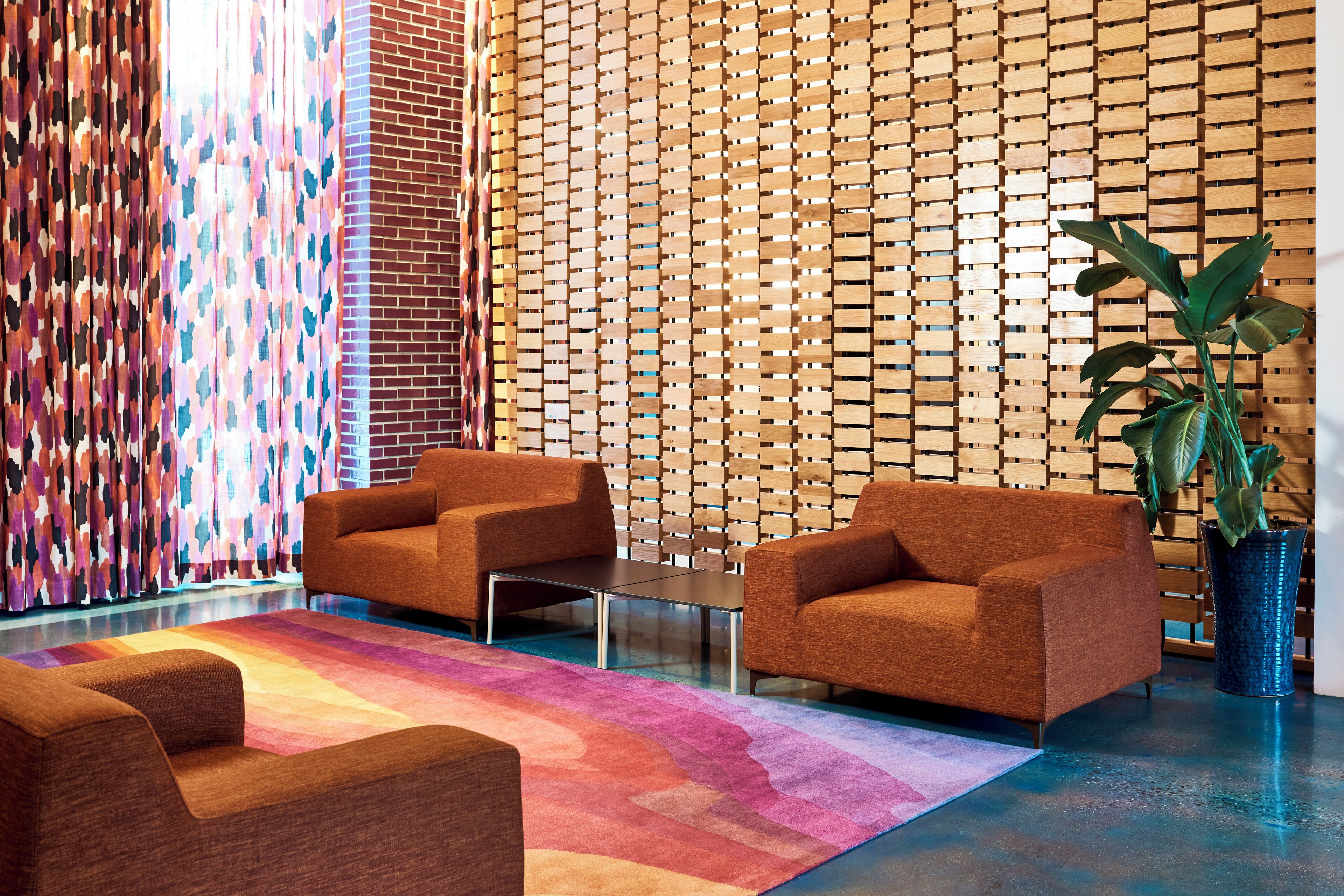 Eine moderne Lobby mit zwei Sofas, einem Couchtisch, einem gemusterten Teppich und einer Holzwand mit geometrischem Muster.
