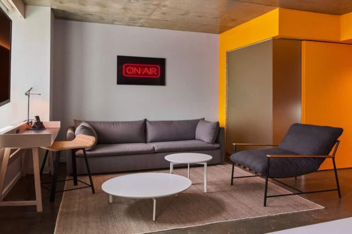 A modern living room with a grey sofa, a black armchair, a small white table, and a 'ON AIR' sign on the wall.
