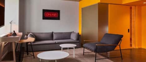 A modern living room with a grey sofa, a black armchair, a small white table, and a 'ON AIR' sign on the wall.