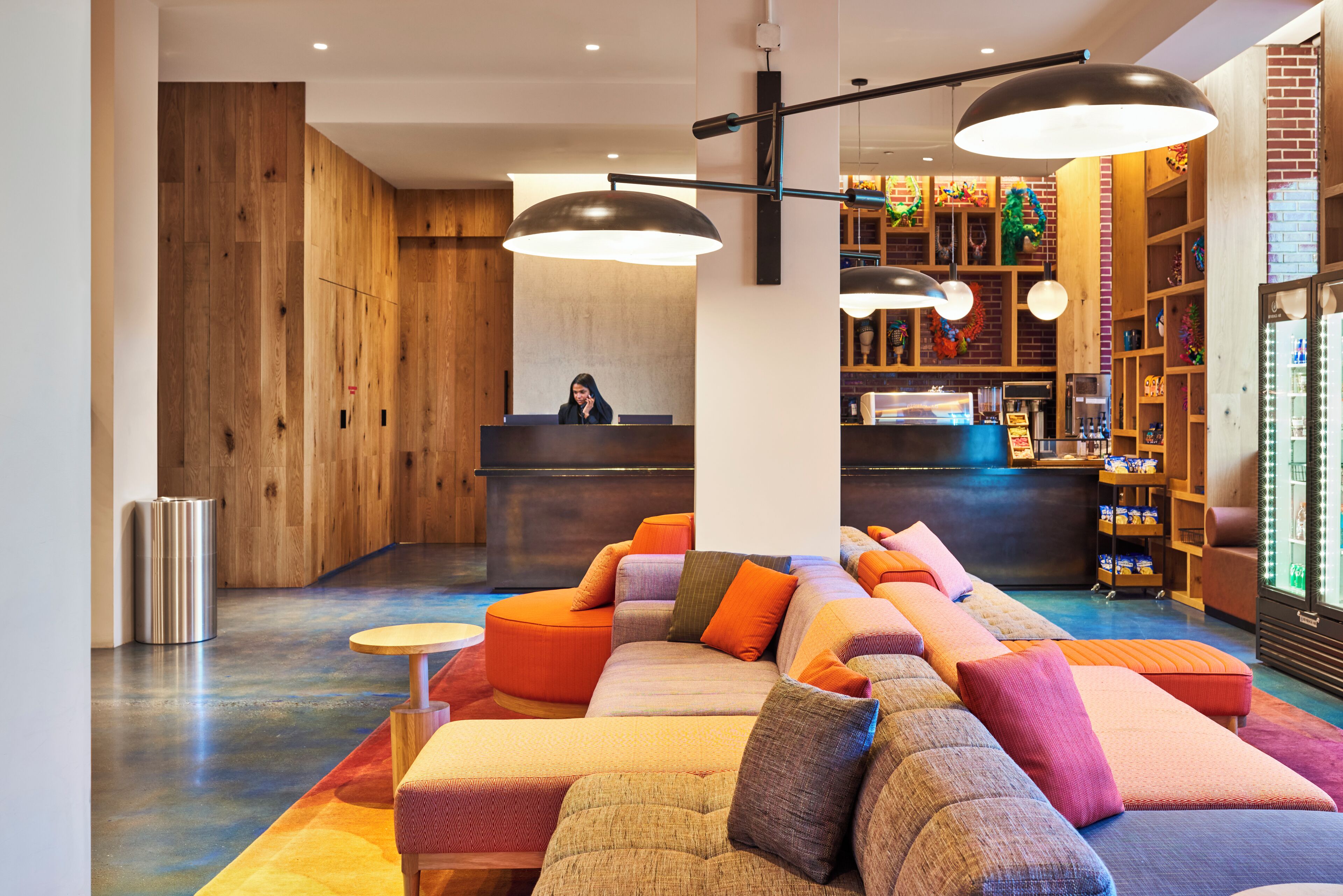 Um lobby moderno com balcão de recepção, área de estar colorida e diversos serviços, incluindo máquina de café e objetos decorativos.