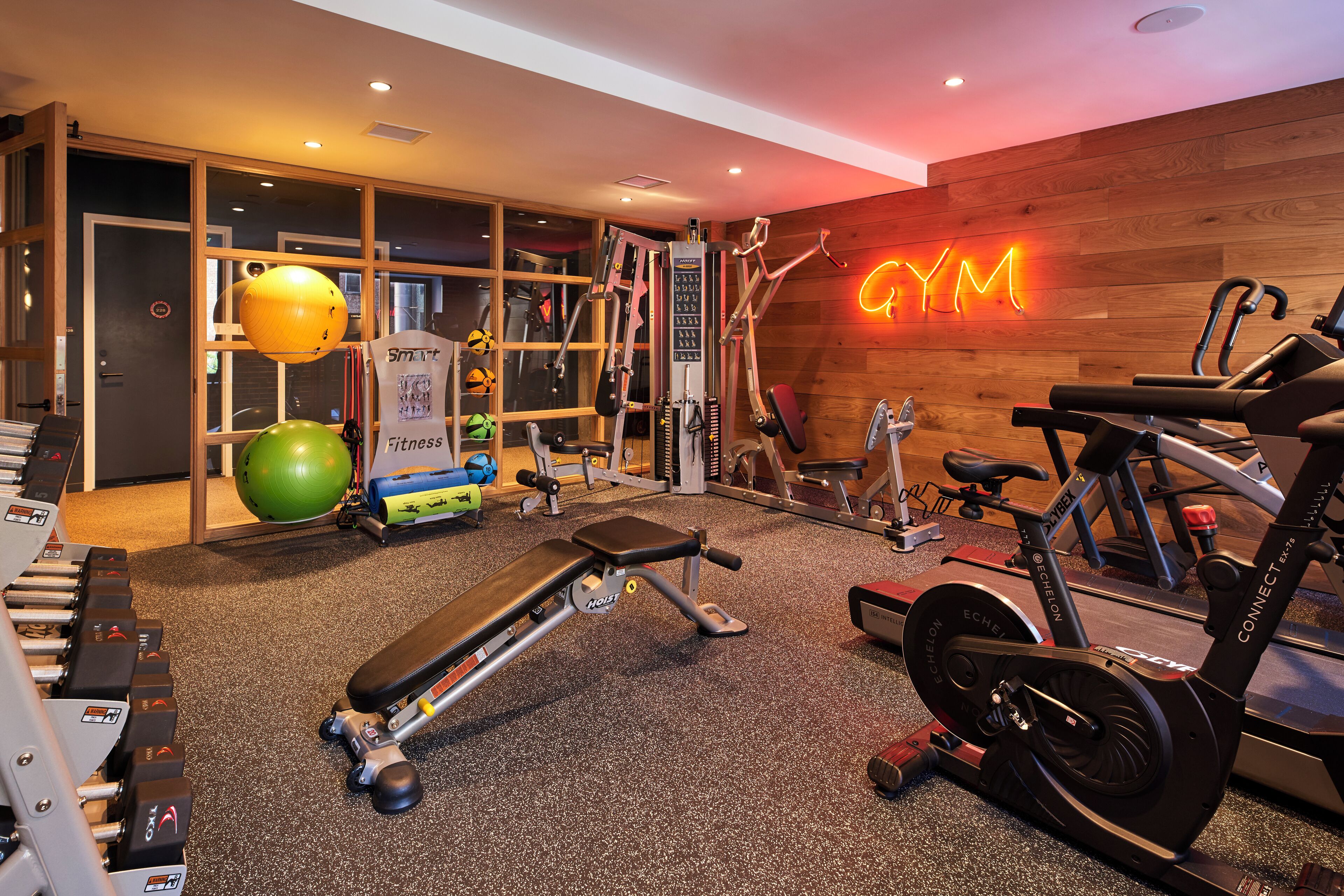 Ein Fitnessstudio mit Trainingsgeräten, einer Neonreklame und einer Holzwand.