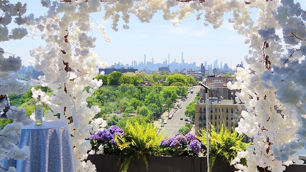 Un'area esterna con un arco fiorito bianco, un tavolo con una bottiglia e vista sullo skyline di una città.
