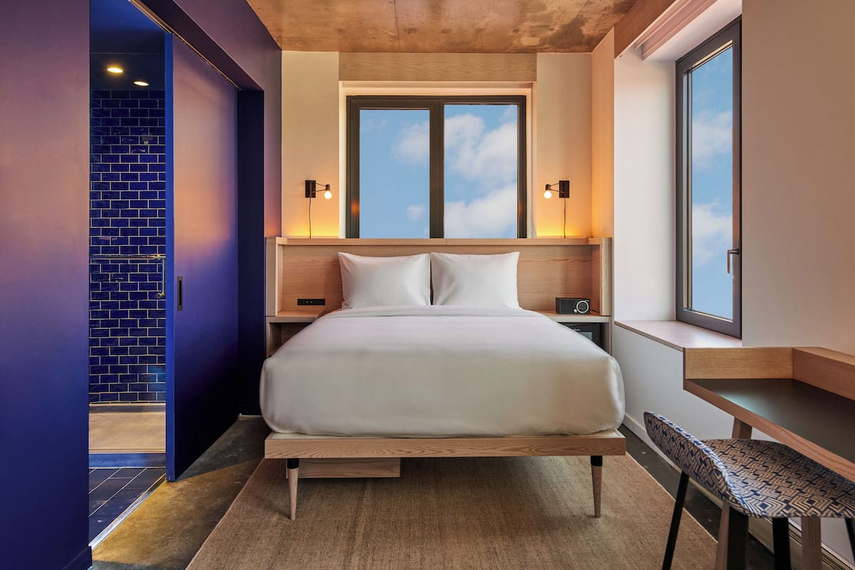 A modern bedroom with a large bed, bedside tables, a desk, and a window with a view.