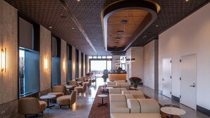 Una hall d'albergo moderna con un'area salotto dalle linee curve, una reception e un'ampia vetrata che offre vista all'esterno.