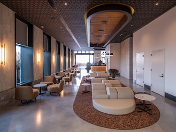 A modern room with a large window, two brown chairs, a small table, and a vase with branches. at Radio Hotel
