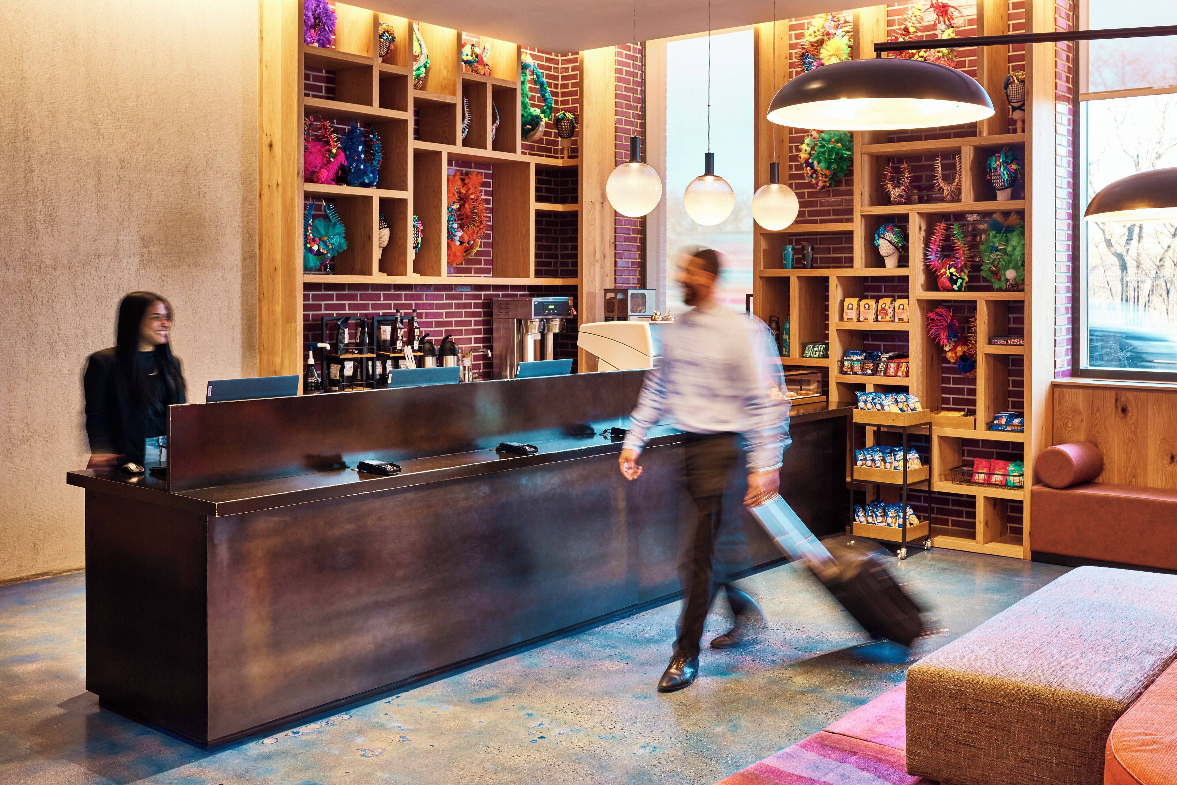 Una moderna área de recepción con un mostrador oscuro, estanterías de madera con decoraciones coloridas e iluminación colgante.