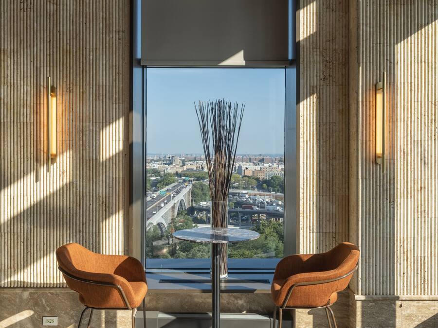 A modern room with a large window, two brown chairs, a small table, and a vase with branches.
