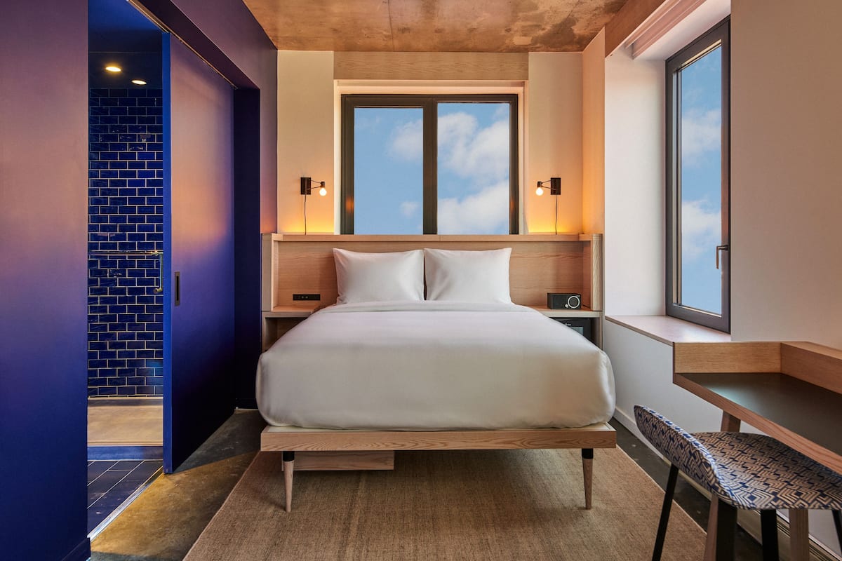 A modern bedroom with a large bed, bedside tables, a window, and a view of the sky.