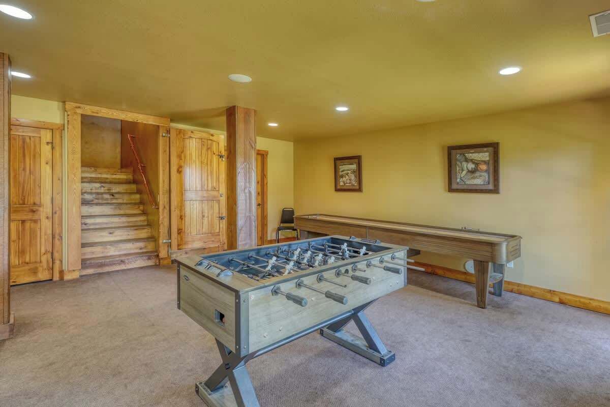 A room with a foosball table, a pool table, and a staircase leading to another area.