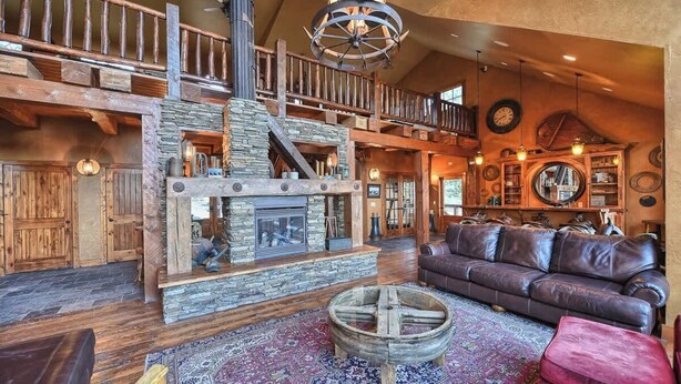 A rustic interior with a stone fireplace, wooden beams, a leather sofa, and a round wooden table. - Foote Creek Lodge (Lead)